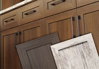 Image showing lower cabinet with five piece laminate (FPL) doors & drawer fronts in a medium brown wood stain with 2 FPL doors angled in front that feature different wood grain finishes